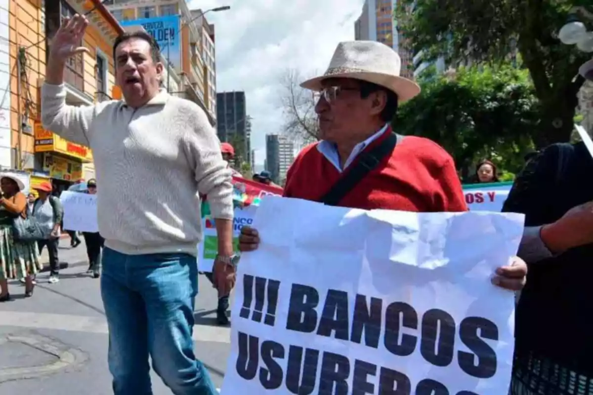 Personas participando en una protesta en la calle, una de ellas sostiene un cartel que dice 