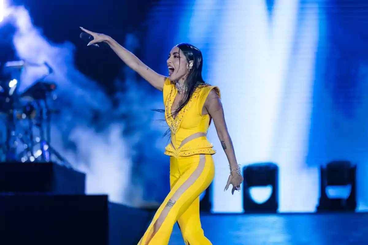 Una cantante en el escenario con un traje amarillo brillante, señalando hacia el público mientras canta apasionadamente.