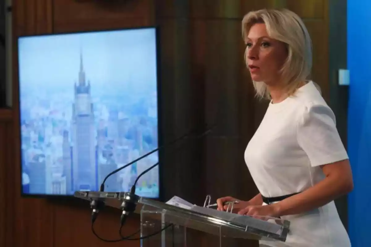 Una persona de pie en un podio hablando con un micrófono y una pantalla de fondo mostrando un edificio alto. Una persona de pie en un podio hablando con un micrófono y una pantalla de fondo mostrando un edificio alto.