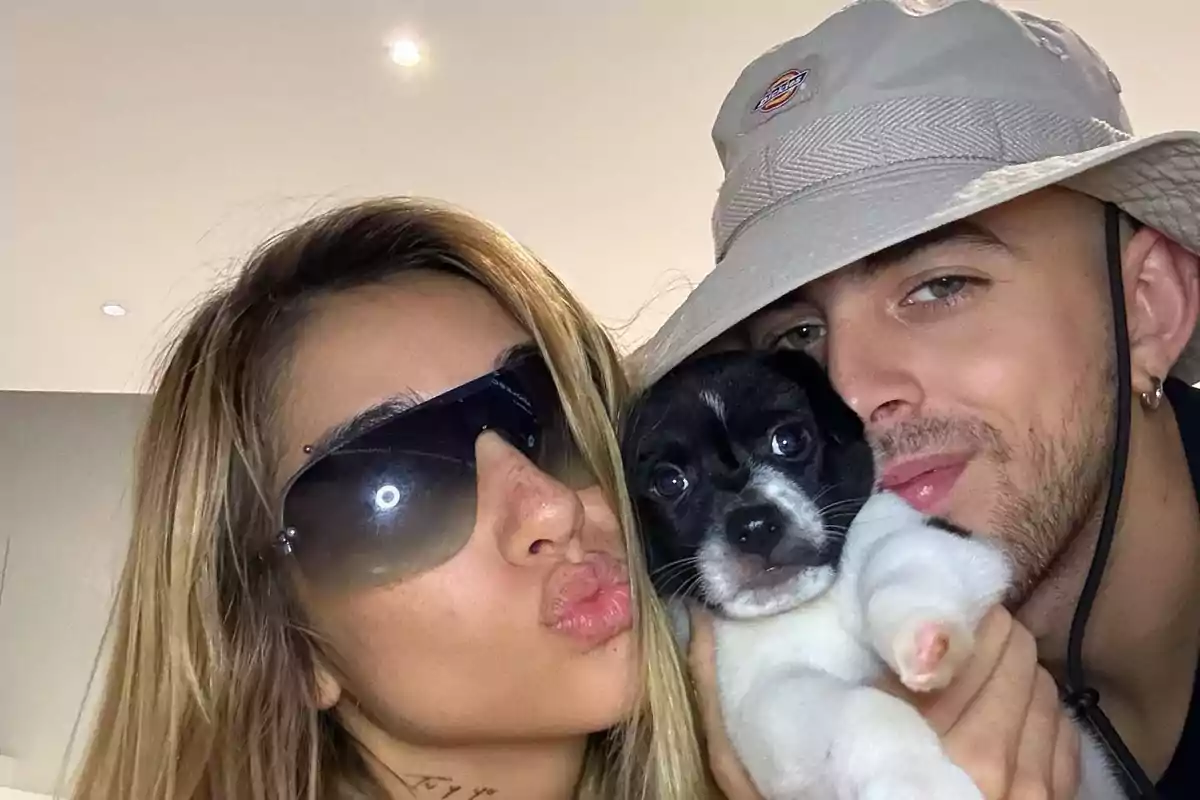 Una pareja sonríe mientras sostiene a un perrito blanco y negro entre ellos Una pareja sonríe mientras sostiene a un perrito blanco y negro entre ellos
