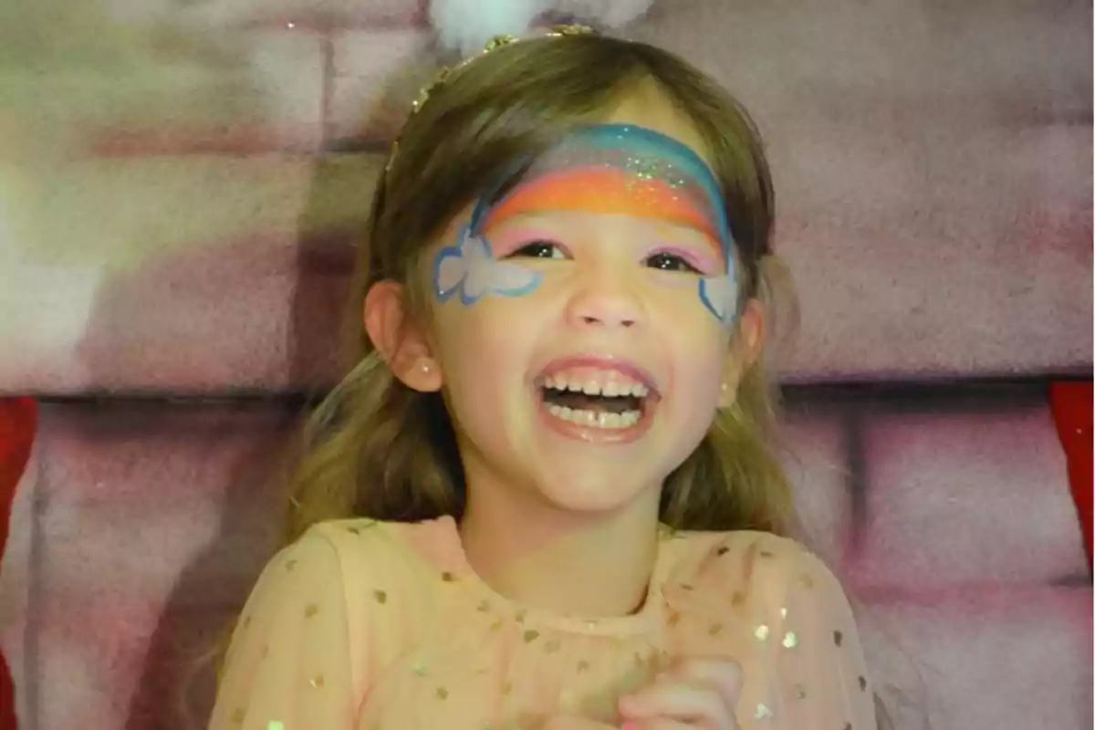 Una niña sonriente con pintura facial de arcoíris y nubes. Una niña sonriente con pintura facial de arcoíris y nubes.
