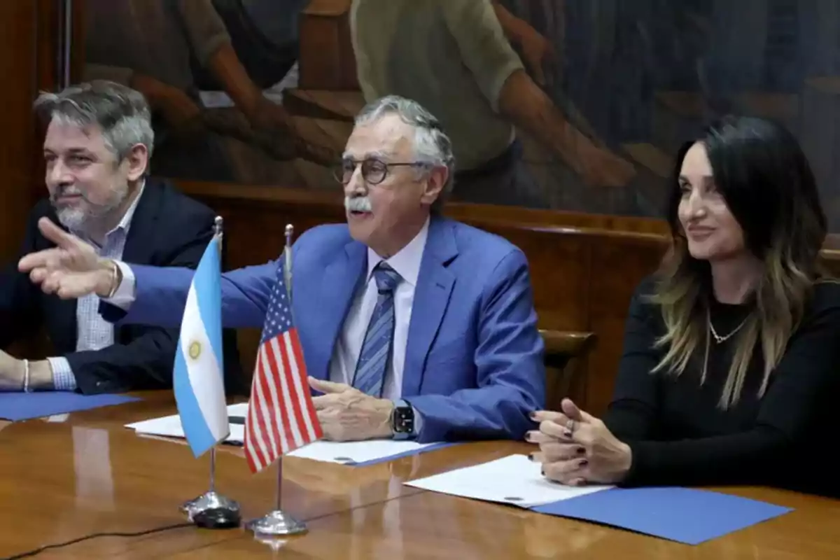 Tres personas sentadas en una mesa de reuniones con banderas de Argentina y Estados Unidos sobre la mesa Tres personas sentadas en una mesa de reuniones con banderas de Argentina y Estados Unidos sobre la mesa