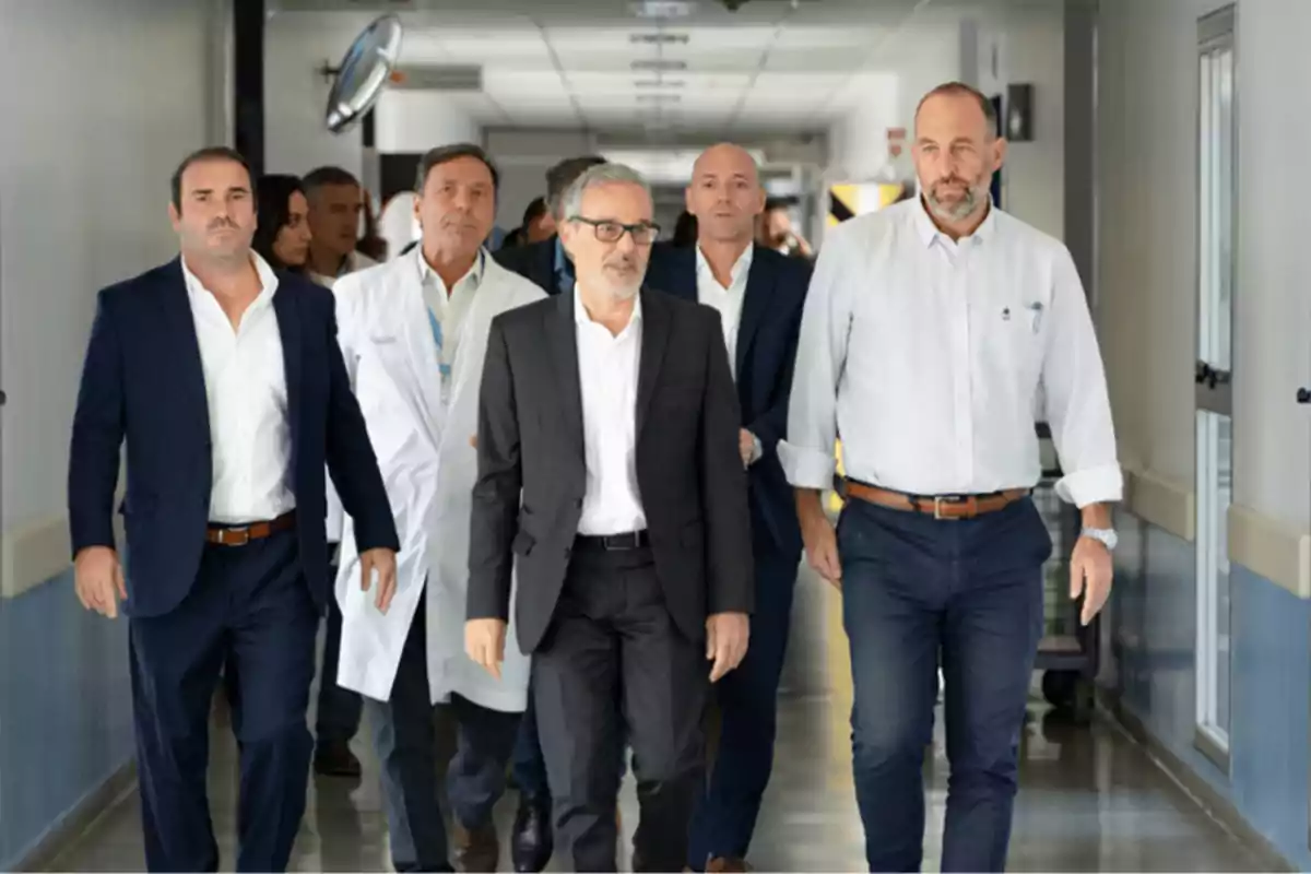 Un grupo de hombres, algunos con trajes y otros con batas de laboratorio, caminan por un pasillo de un edificio.