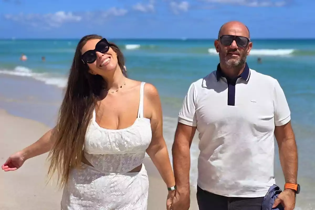 Pareja sonriente con gafas de sol disfrutando de un día soleado en la playa con el mar de fondo