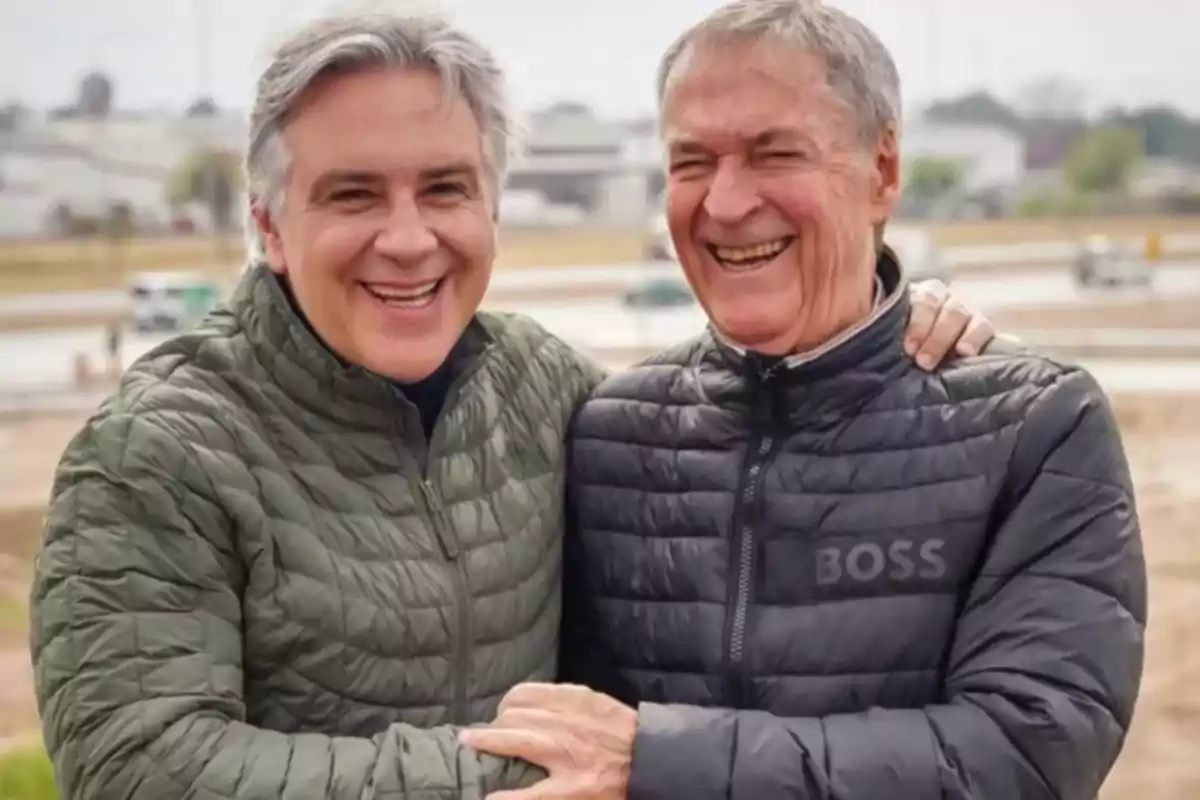 Dos hombres sonrientes con camperas acolchadas se abrazan al aire libre Dos hombres sonrientes con camperas acolchadas se abrazan al aire libre