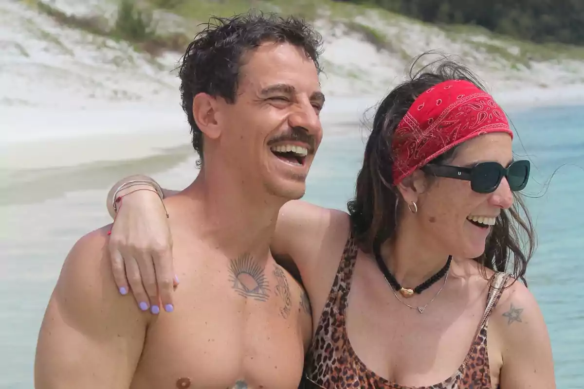 Una pareja sonriente disfruta de un día soleado en la playa con el mar de fondo.