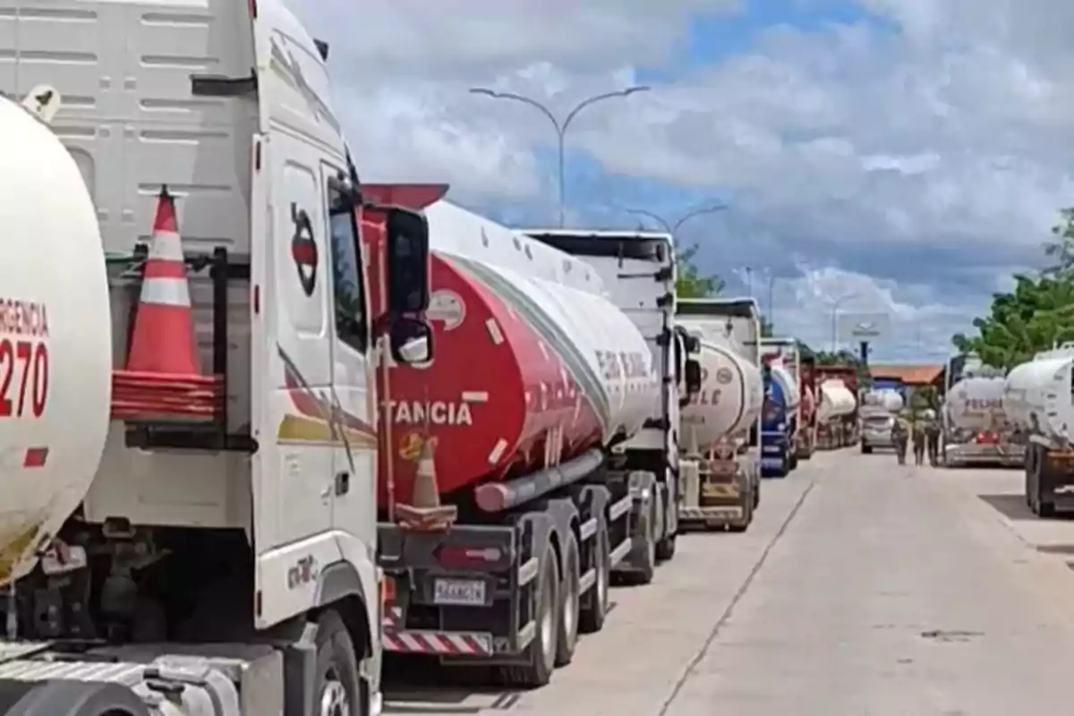 A row of tanker trucks parked on a road under a cloudy sky.