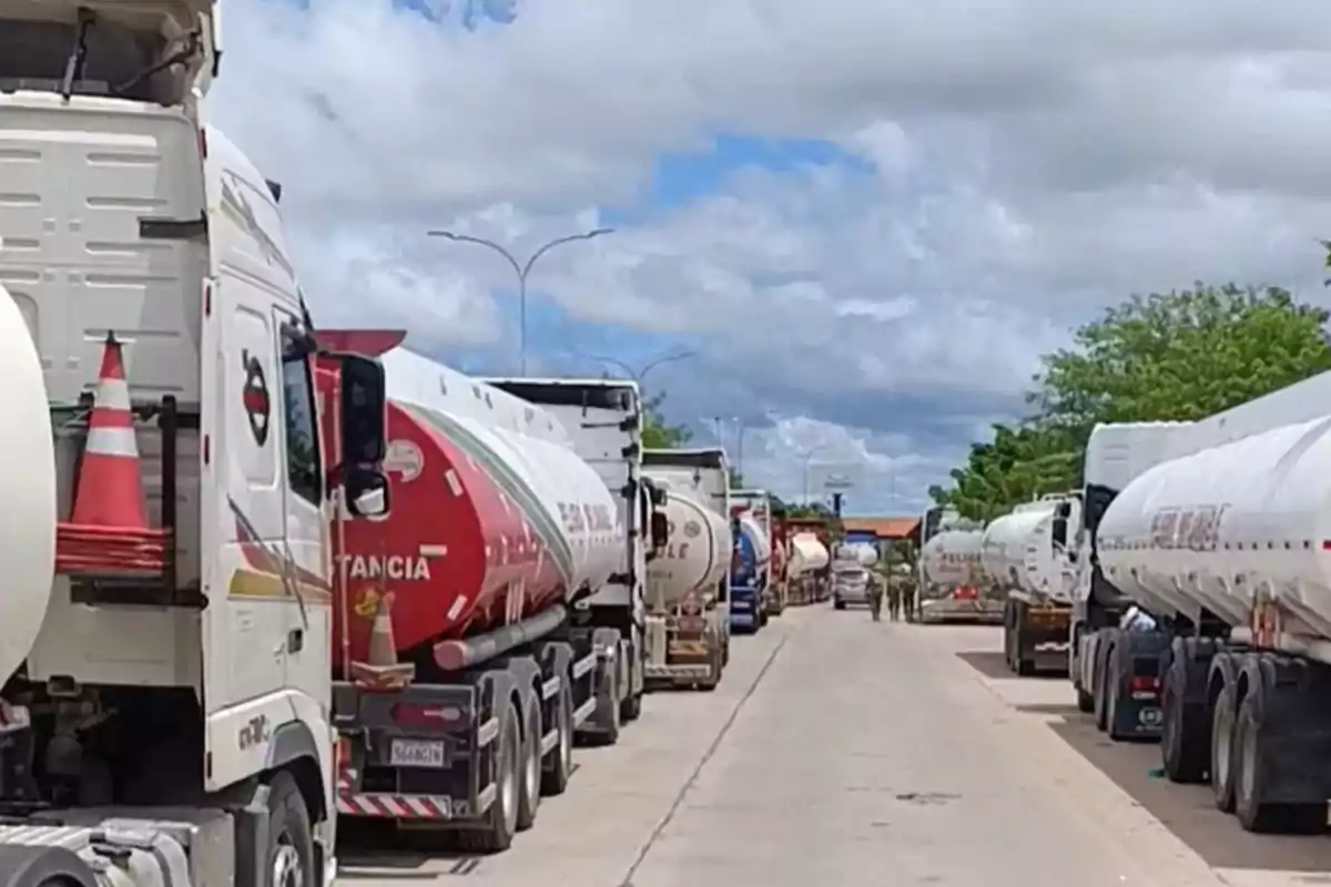 Una fila de camiones cisterna estacionados en una carretera bajo un cielo nublado.