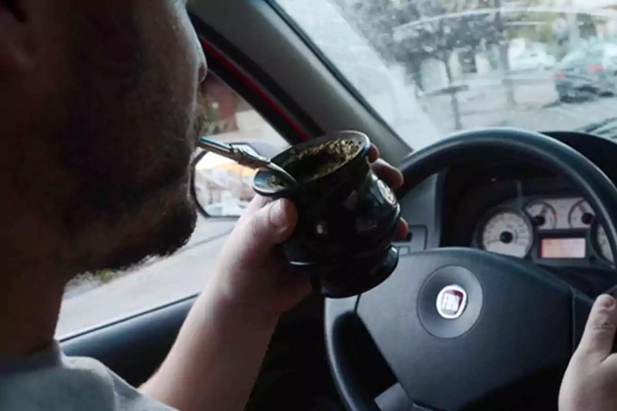 Person driving a car while holding a mate in their left hand. Person driving a car while holding a mate in their left hand.