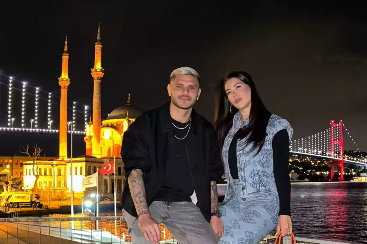 Una pareja posando frente a un puente iluminado y una mezquita en Estambul durante la noche.