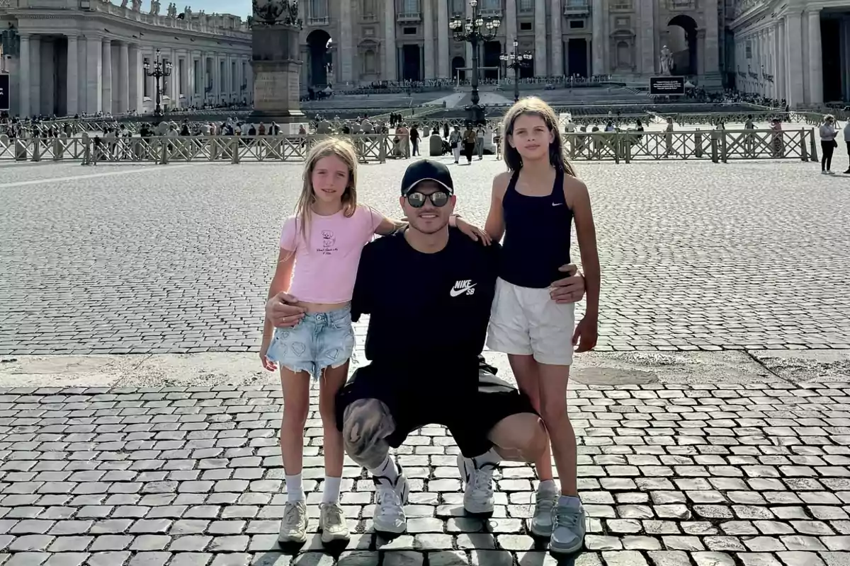A man with two girls poses together in a cobblestone square in front of a historic building with columns and a large facade.