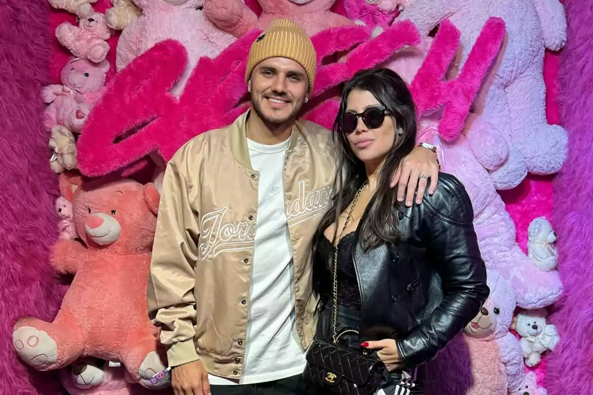 Una pareja posa frente a un fondo decorado con osos de peluche rosas y letras grandes de color fucsia.