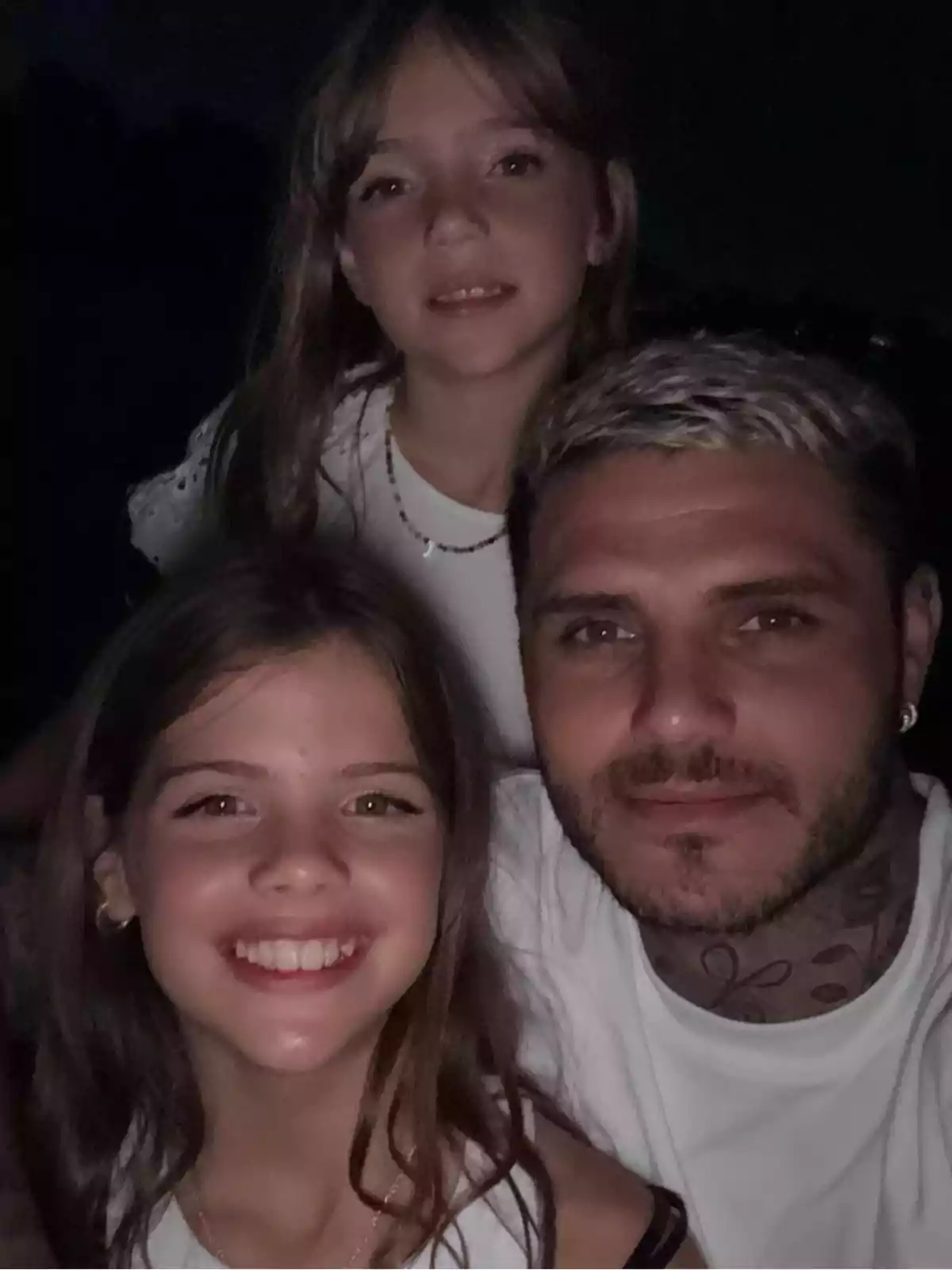 A man and two girls smile together in a selfie taken at night. A man and two girls smile together in a selfie taken at night.