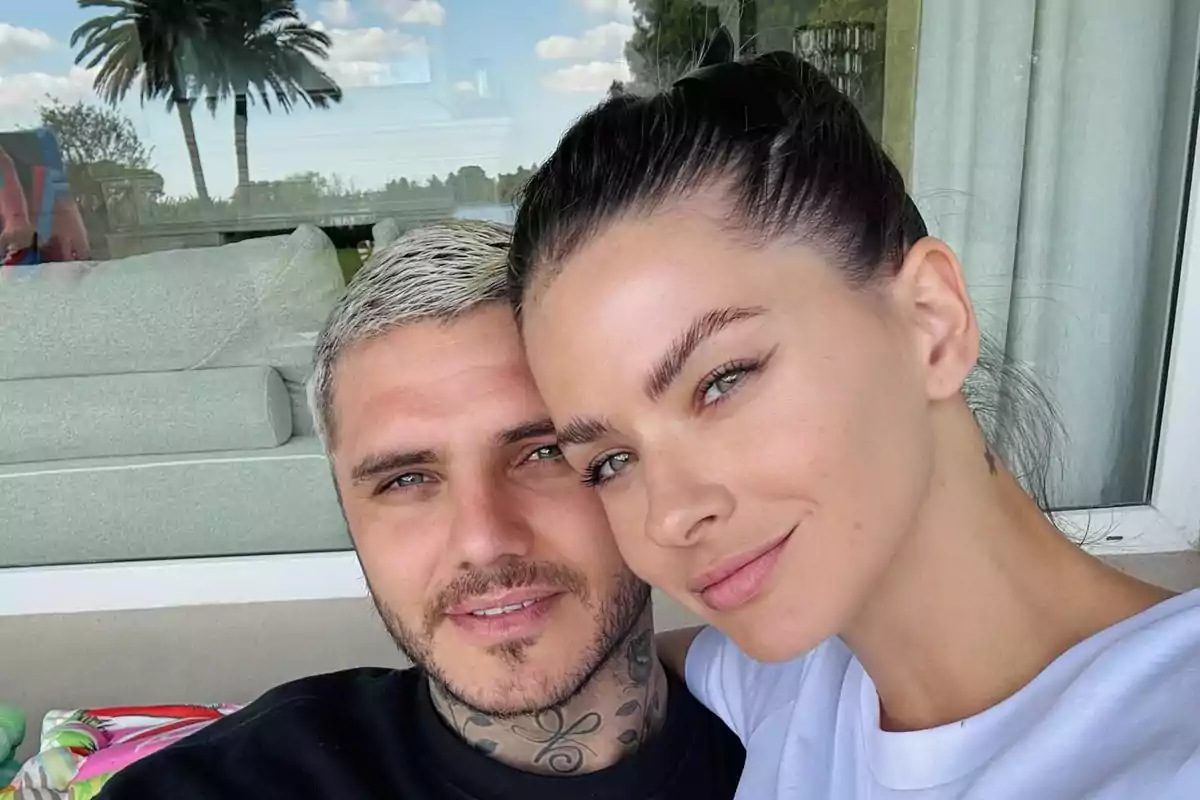 Una pareja sonriente se toma una selfie al aire libre con un fondo de cielo azul y palmeras.