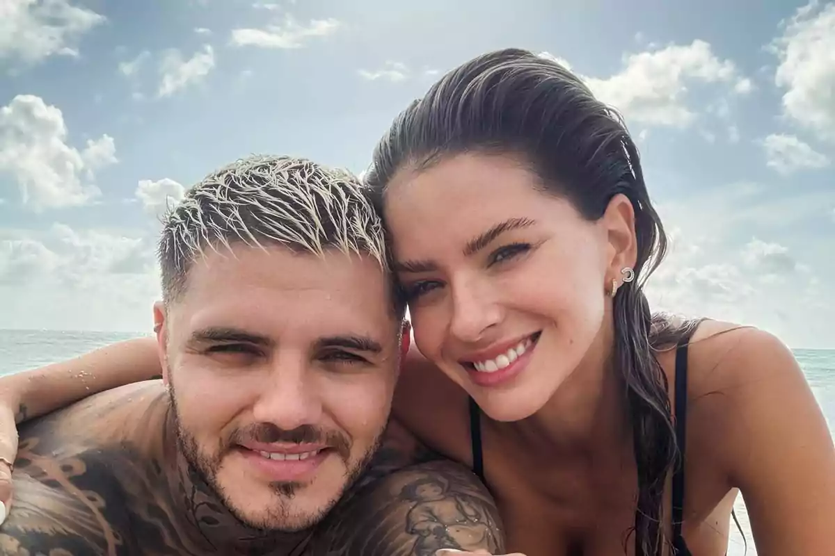 Pareja joven sonriendo y posando juntos en la playa con el mar y el cielo nublado de fondo Pareja joven sonriendo y posando juntos en la playa con el mar y el cielo nublado de fondo
