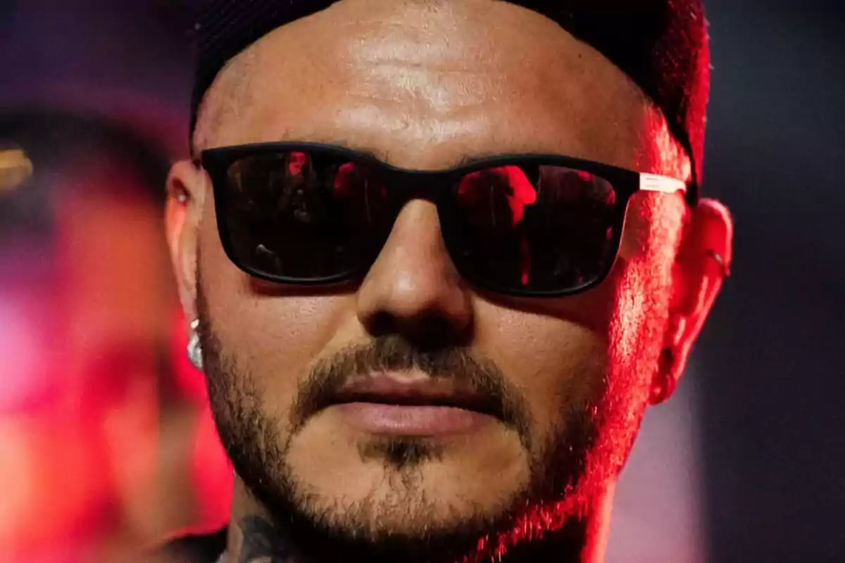 Man with sunglasses and a cap in a red-lit environment.
