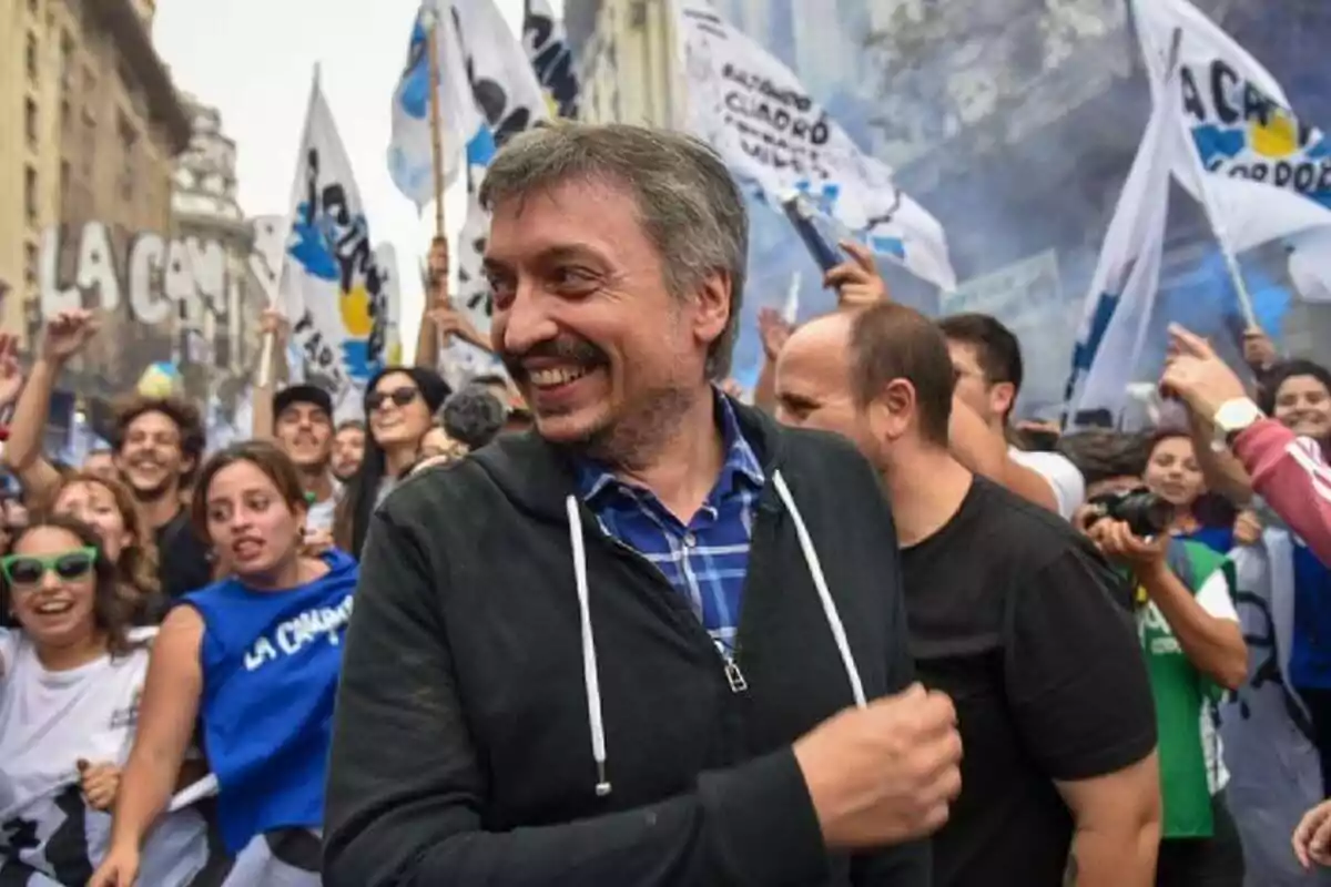 Un hombre sonriente en una multitud de personas con banderas y pancartas en una manifestación en una ciudad.