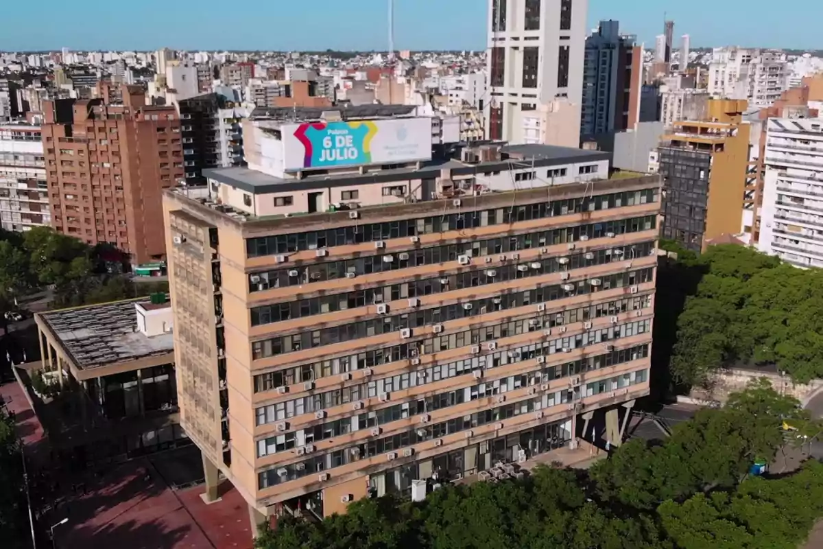 Edificio alto con múltiples ventanas y unidades de aire acondicionado en una ciudad con otros edificios alrededor.