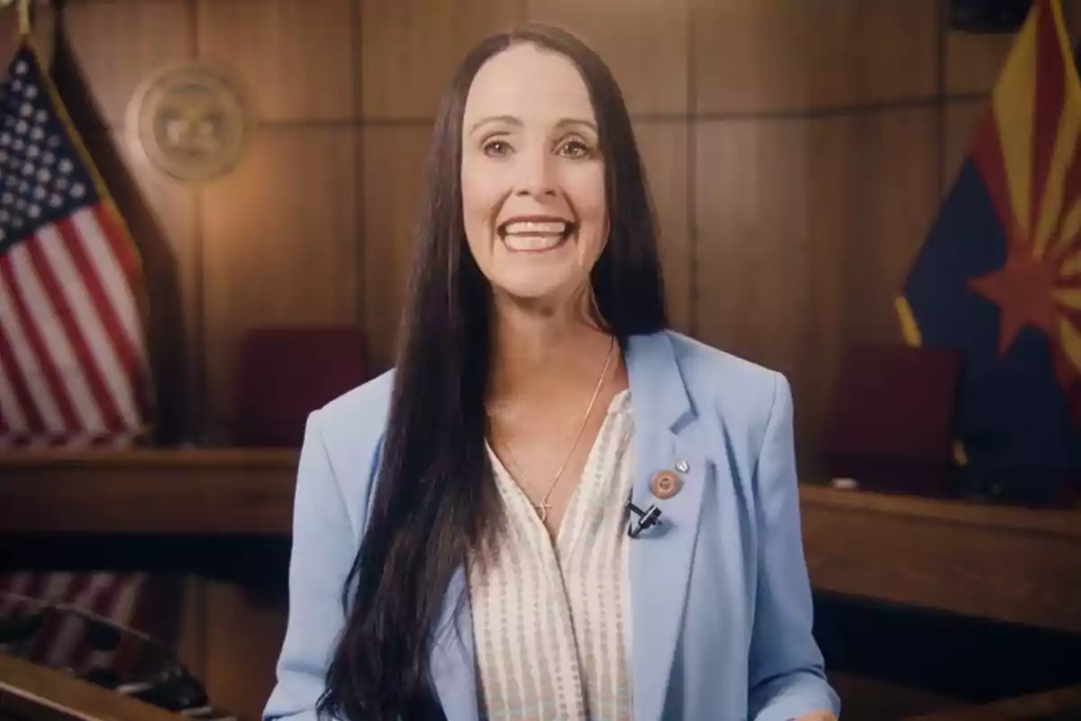 Woman with long dark hair smiles in front of a room with United States and Arizona flags in the background Woman with long dark hair smiles in front of a room with United States and Arizona flags in the background