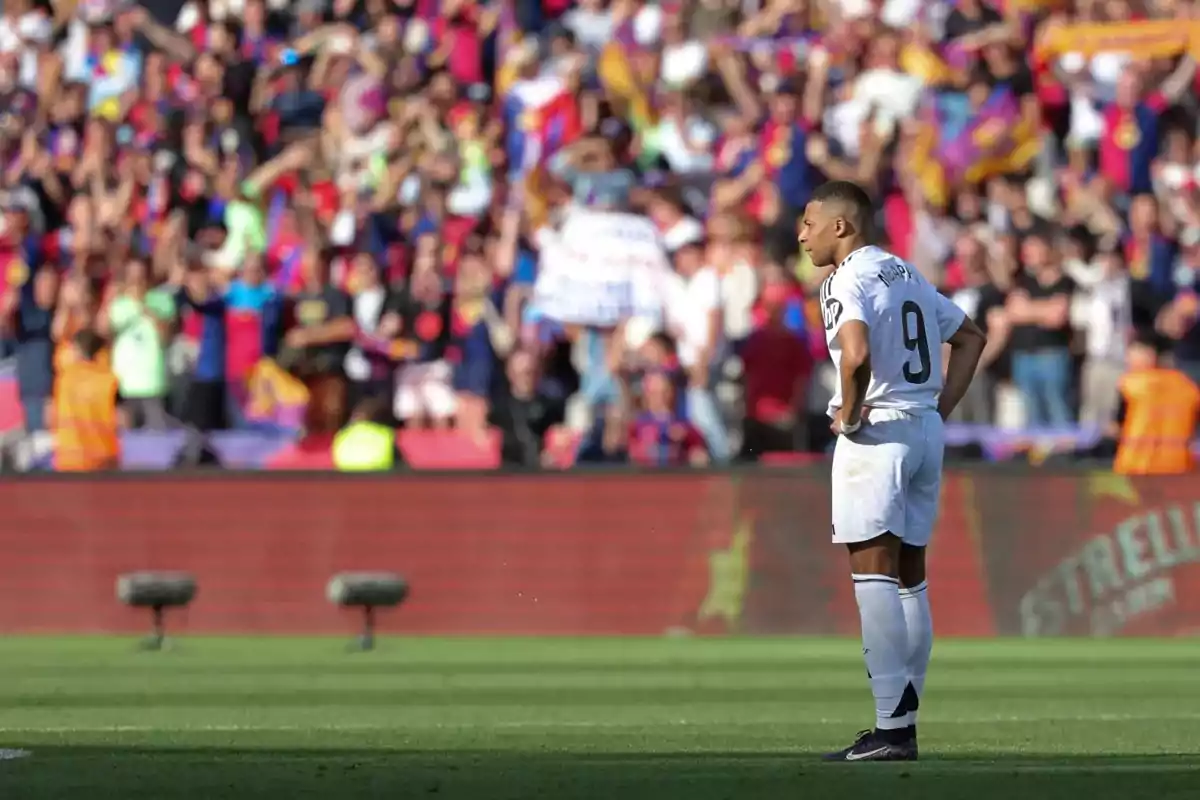 Jugador de fútbol con uniforme blanco en el campo mientras el público en las gradas observa.