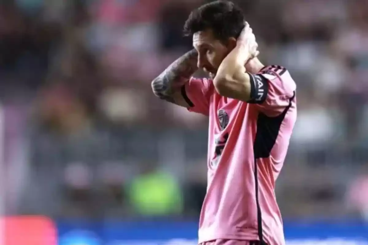 Un jugador de fútbol con uniforme rosa se lleva las manos a la cabeza en el campo de juego.