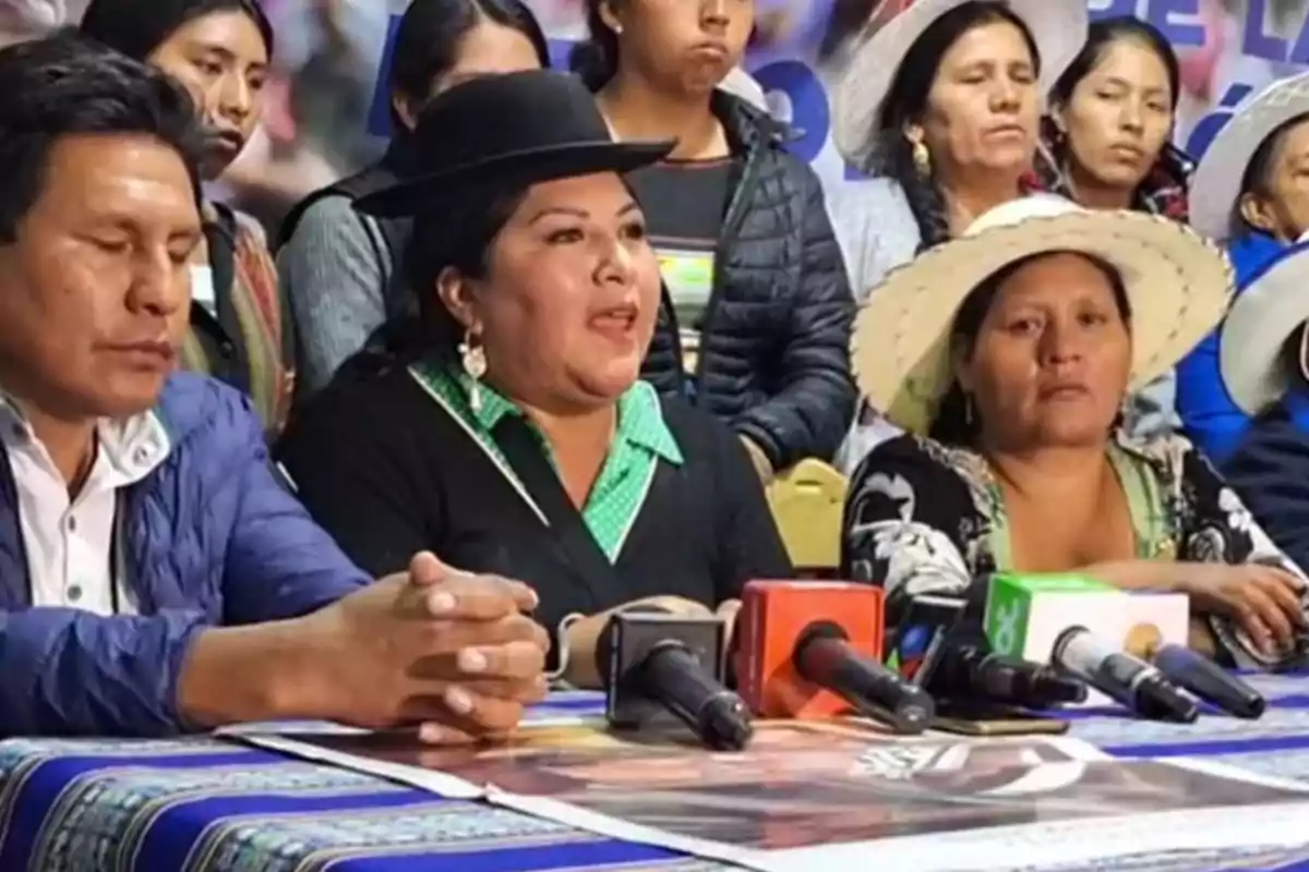 Un grupo de personas en una conferencia de prensa con micrófonos y carteles en una mesa.