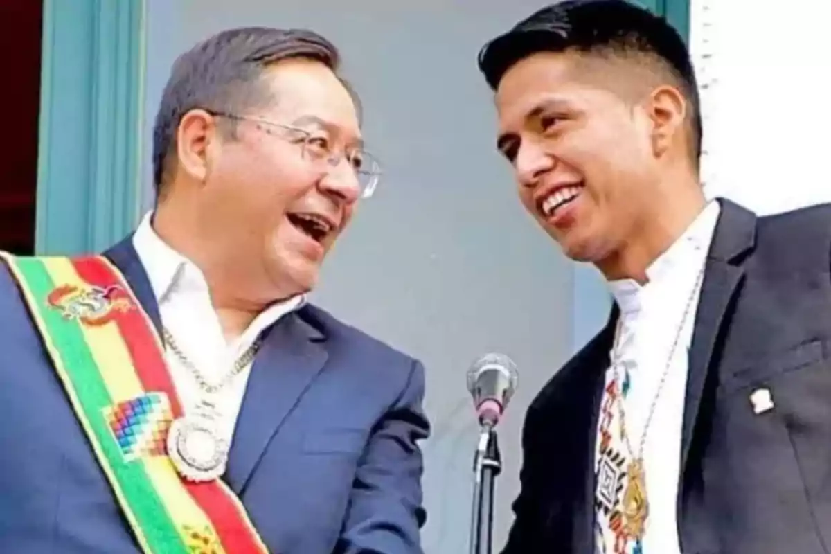 Dos hombres sonríen mientras conversan frente a un micrófono, uno lleva una banda presidencial. Dos hombres sonríen mientras conversan frente a un micrófono, uno lleva una banda presidencial.