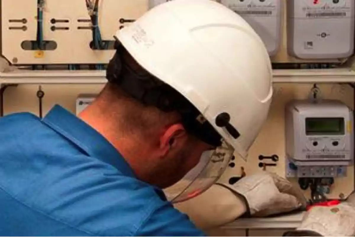 Worker with a hard hat and gloves inspecting an electric meter panel Worker with a hard hat and gloves inspecting an electric meter panel