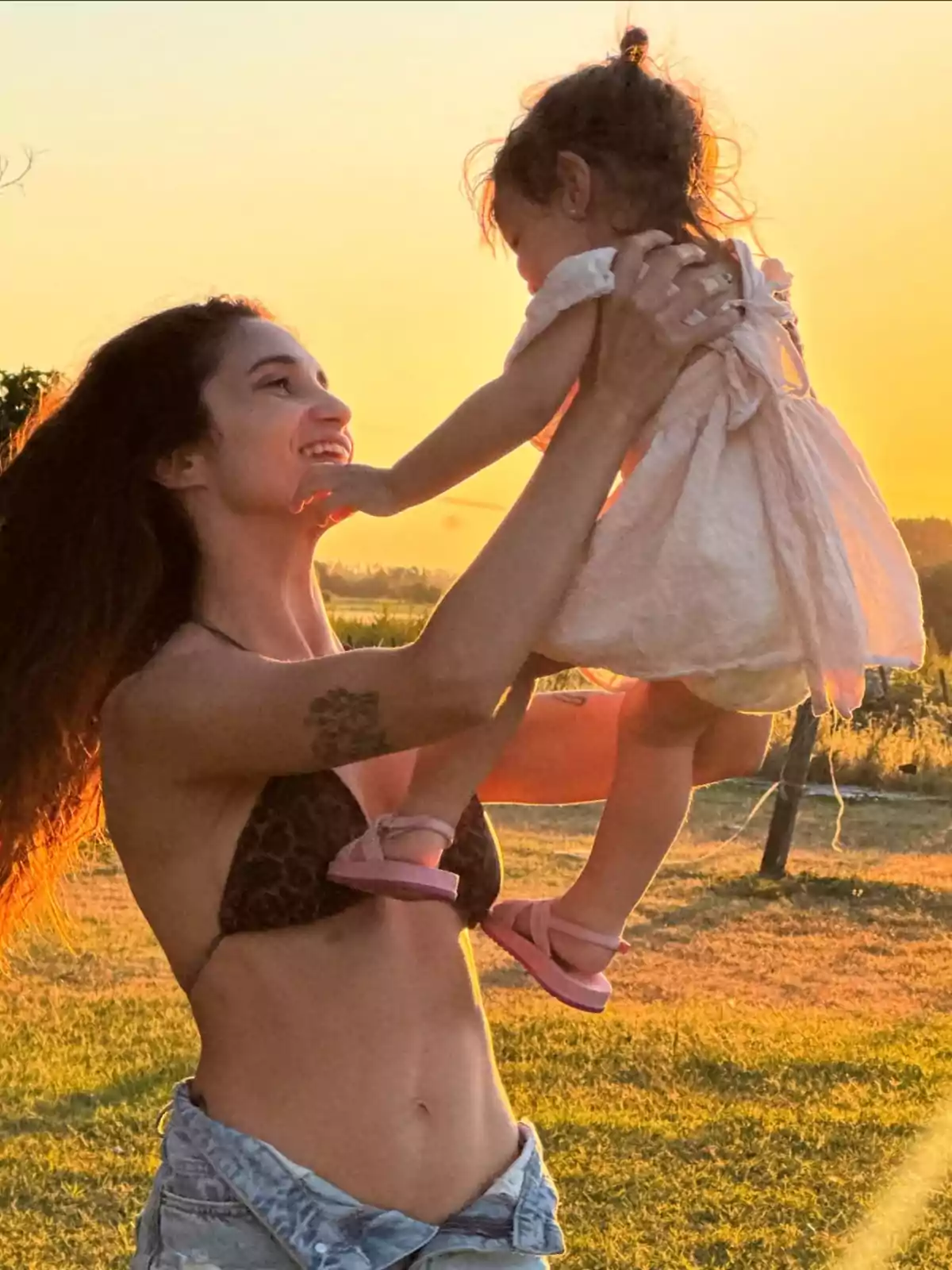 A smiling woman lifts a small girl in her arms at sunset in a field. A smiling woman lifts a small girl in her arms at sunset in a field.