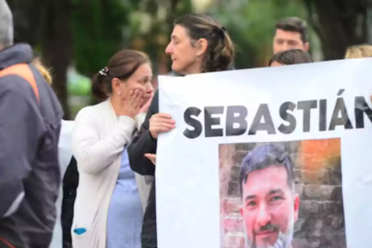 People hold a sign with a man's photo and the name Sebastián while a woman appears visibly moved.