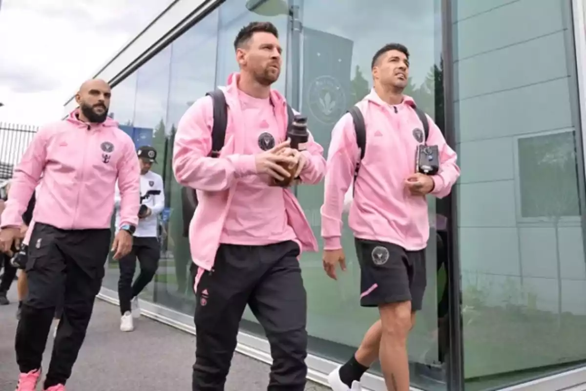 Three players in pink sportswear walk together outside a glass building, carrying backpacks and bottles. Three players in pink sportswear walk together outside a glass building, carrying backpacks and bottles.