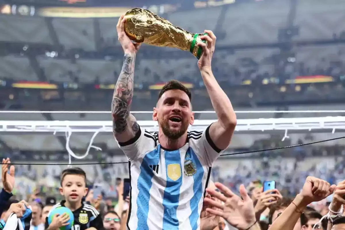 A player wearing the Argentina jersey lifts a golden trophy as the crowd celebrates around him. A player wearing the Argentina jersey lifts a golden trophy as the crowd celebrates around him.