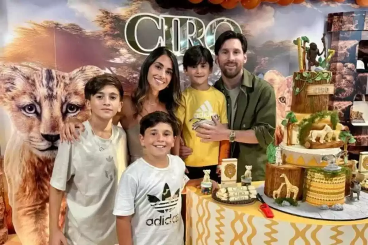 Una familia sonríe frente a una mesa decorada con un pastel temático de animales y el nombre "Ciro" en el fondo.