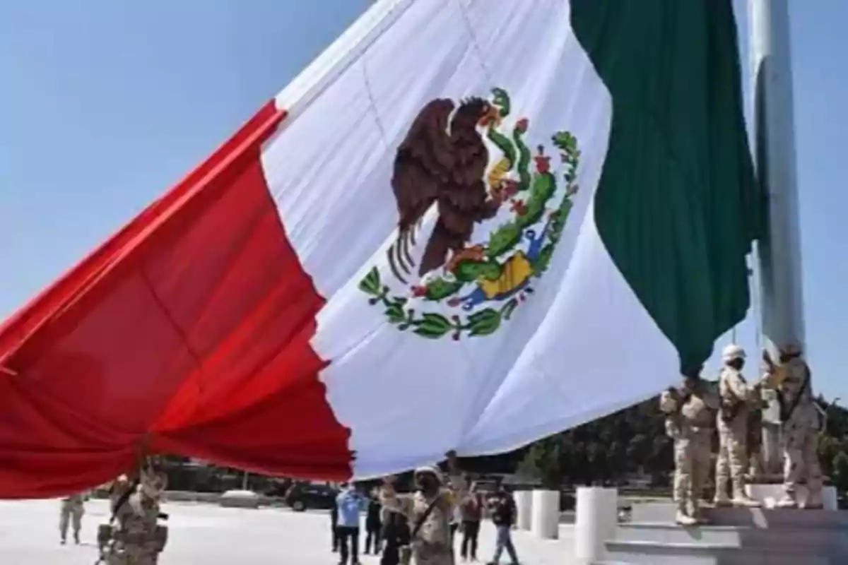 Personas izando una gran bandera de México en un espacio público.