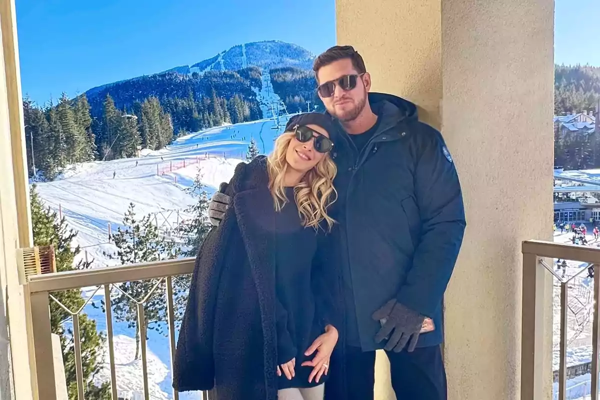 Una pareja con gafas de sol posa en un balcón con un paisaje nevado y montañas al fondo. Una pareja con gafas de sol posa en un balcón con un paisaje nevado y montañas al fondo.