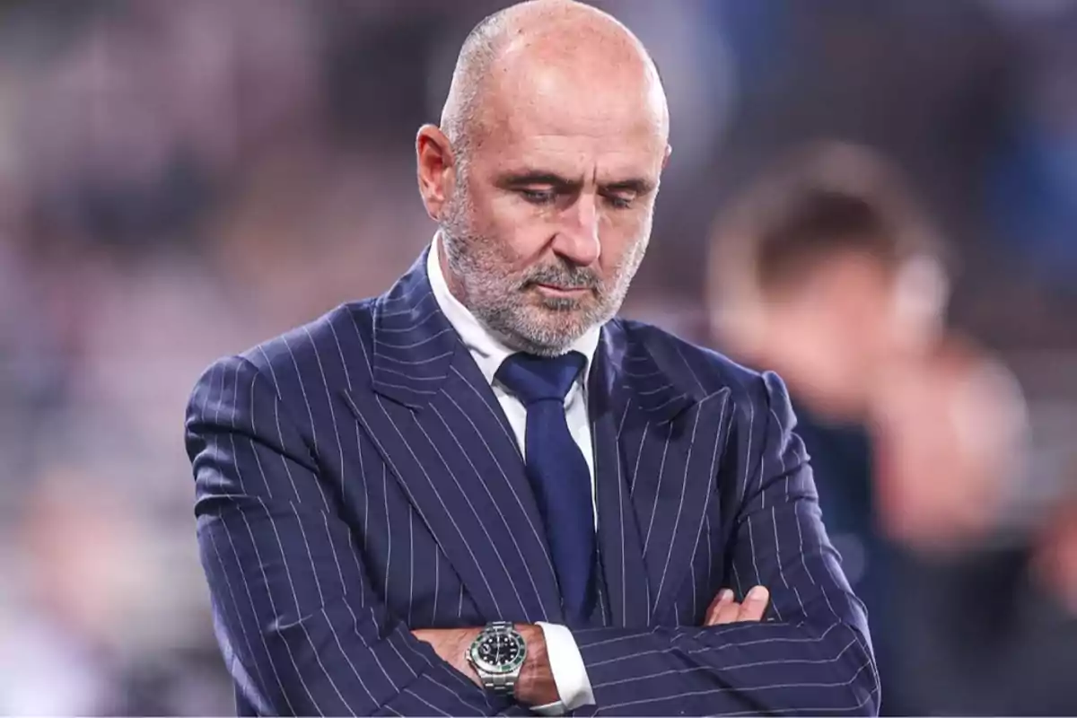 Bald man with a beard and a blue striped suit looking down with a serious expression and his arms crossed Bald man with a beard and a blue striped suit looking down with a serious expression and his arms crossed