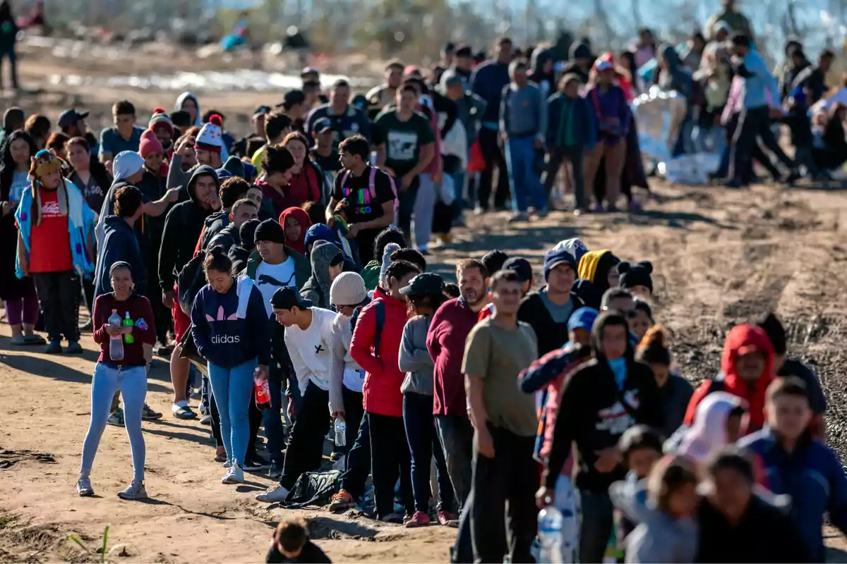 Un grupo numeroso de personas camina en fila por un camino de tierra en un entorno al aire libre.