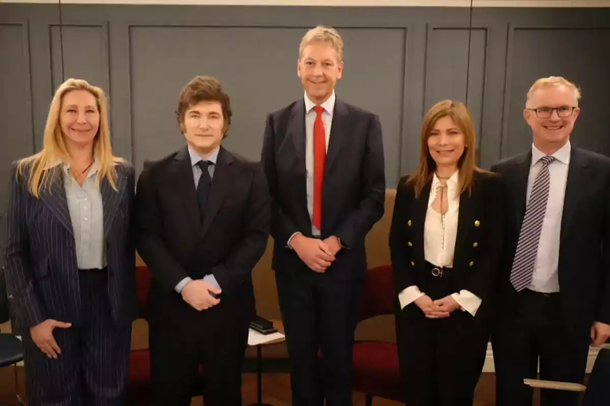 Un grupo de cinco personas vestidas de manera formal posando para una foto en un entorno interior.