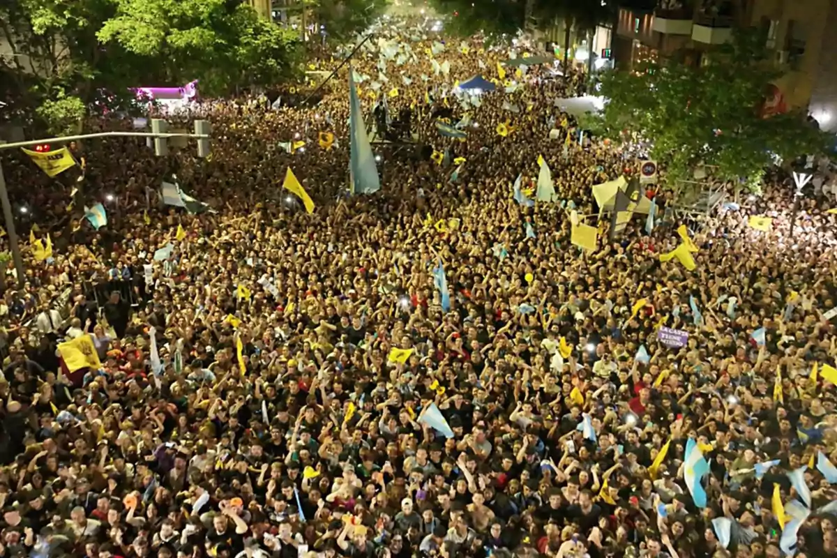 Crowd of people gathered at a nighttime street protest, many of them holding flags and banners Crowd of people gathered at a nighttime street protest, many of them holding flags and banners