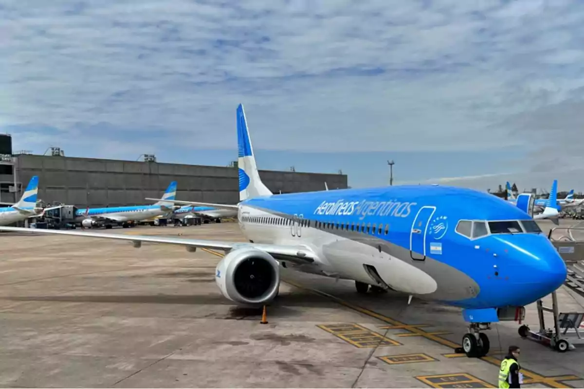 Avión de Aerolíneas Argentinas en el aeropuerto con otros aviones en el fondo y un cielo parcialmente nublado