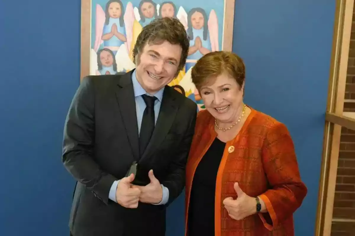 Dos personas sonrientes posan juntas frente a una pintura colorida en un fondo azul.