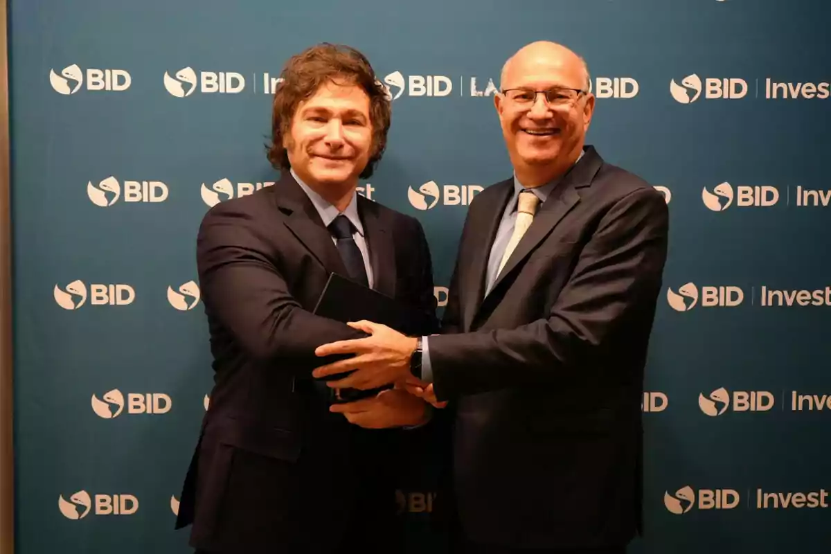 Dos hombres de traje se dan la mano frente a un fondo con el logotipo del BID.