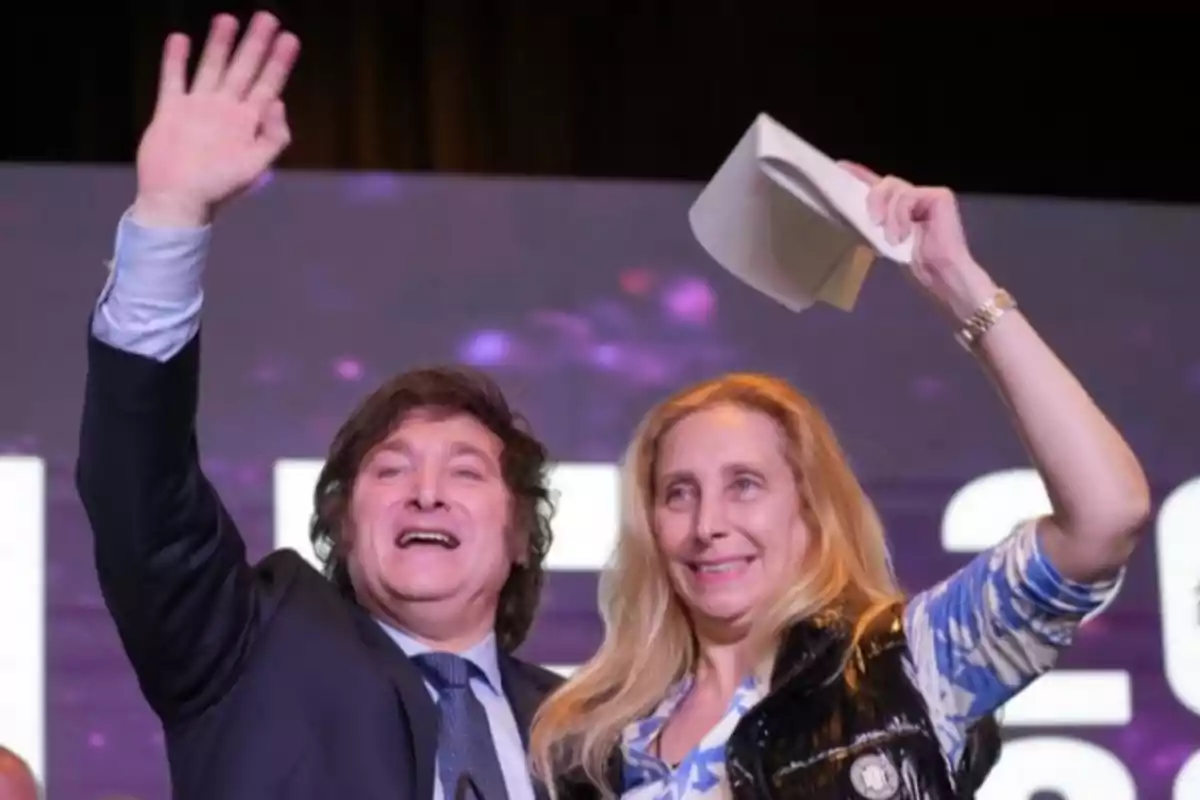 Two people smile and wave their hands at an event. Two people smile and wave their hands at an event.