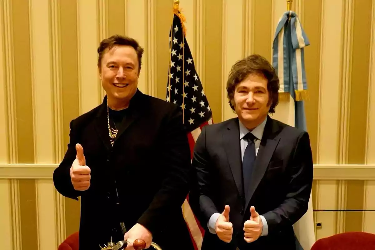 Dos hombres sonrientes posan juntos haciendo el gesto de pulgar arriba con banderas de Estados Unidos y Argentina de fondo