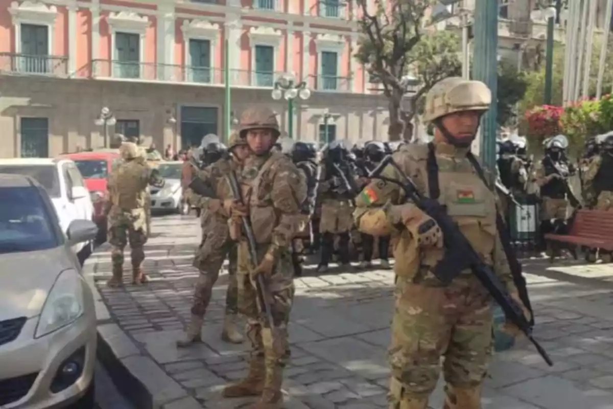 Soldados con uniforme militar y equipo de protección están de pie en una calle empedrada frente a un edificio histórico, mientras otros militares y vehículos se observan en el fondo. Soldados con uniforme militar y equipo de protección están de pie en una calle empedrada frente a un edificio histórico, mientras otros militares y vehículos se observan en el fondo.