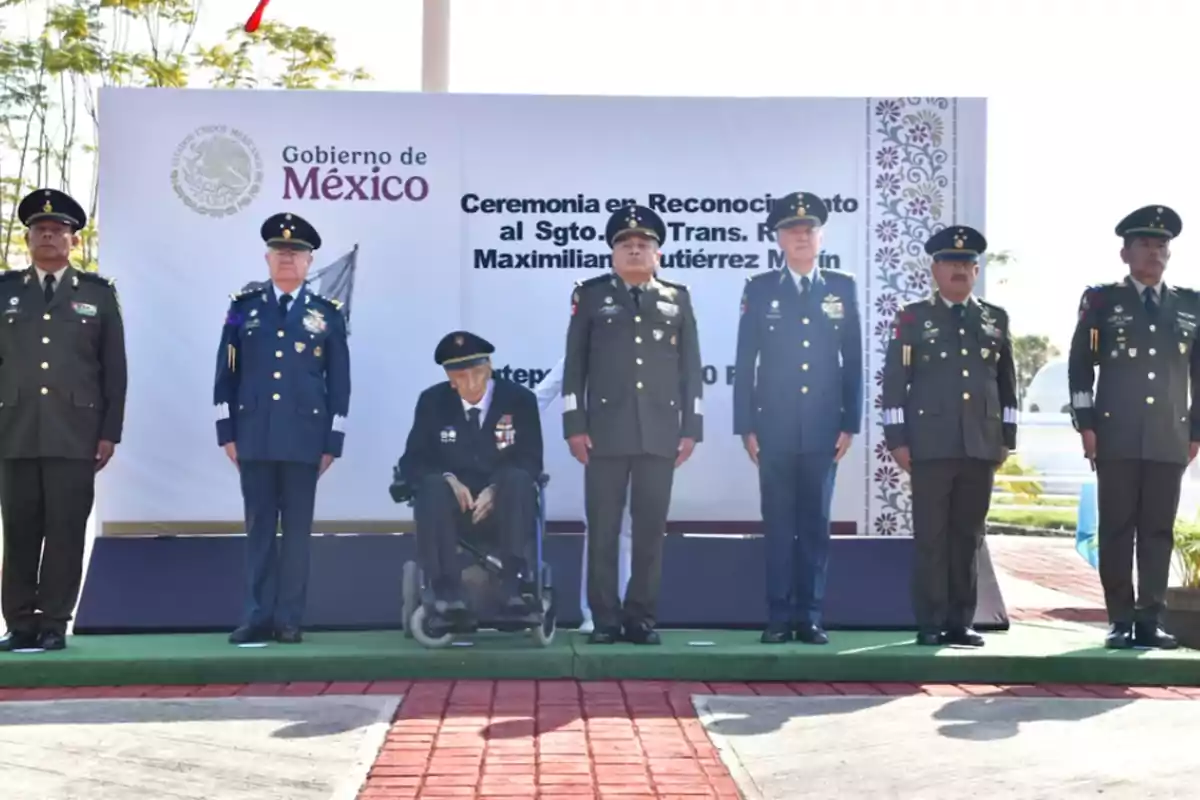 Un grupo de militares en uniforme de gala se encuentra de pie en una ceremonia oficial en México, con un fondo que muestra un cartel del gobierno. Un grupo de militares en uniforme de gala se encuentra de pie en una ceremonia oficial en México, con un fondo que muestra un cartel del gobierno.
