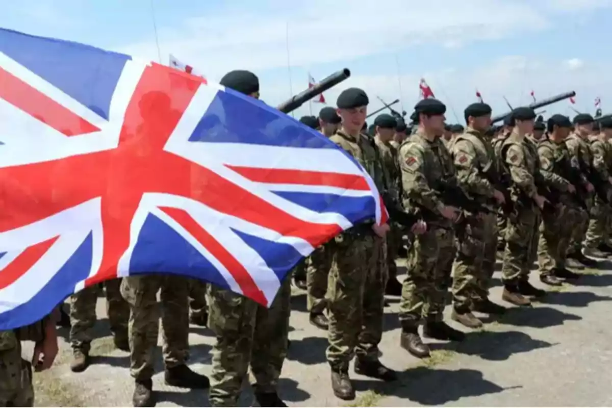 Soldados en formación con uniforme militar y una bandera del Reino Unido ondeando al frente.