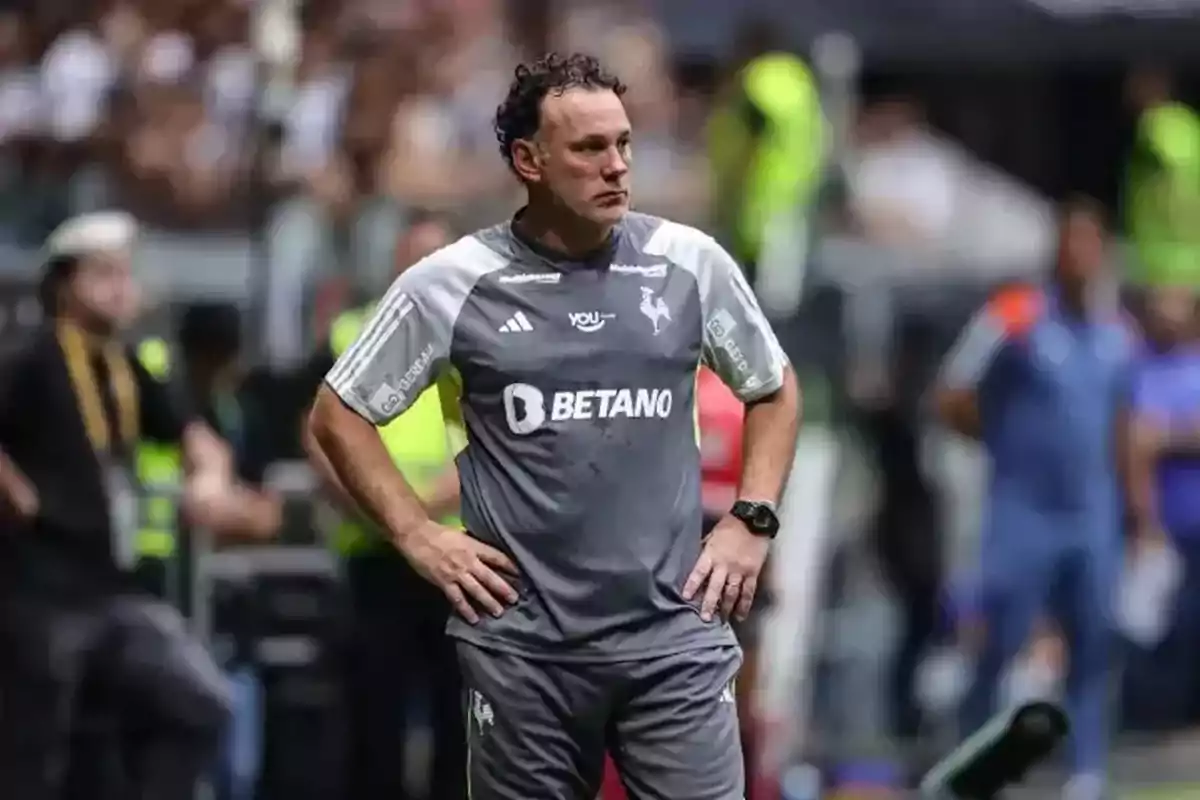 A man in a gray sports uniform is standing with his hands on his hips in a sports setting. A man in a gray sports uniform is standing with his hands on his hips in a sports setting.