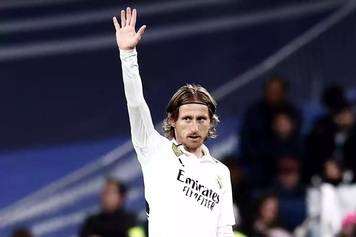 A player in a white uniform raises his hand in a stadium.