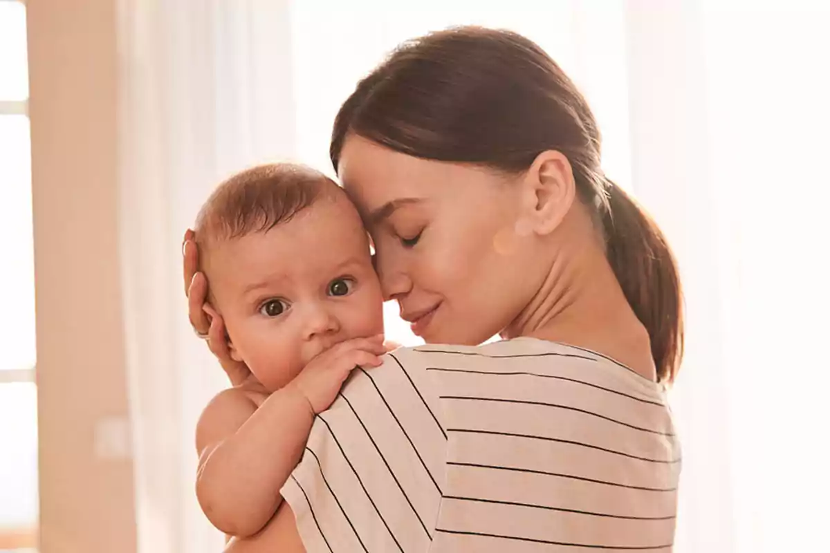 A woman holding a baby in her arms with an expression of tenderness and love.